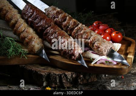 Gros plan d'un plat traditionnel caucasien – assortiment de viande hachée grillée (lula kebab ou shish kebab) sur des brochettes en métal. Avec des kebabs fabriqués à partir de chi Banque D'Images