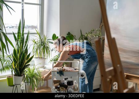 Femme peintre travaillant sur l'image dans le home studio créatif, en utilisant des matériaux et des outils pour la peinture. Banque D'Images
