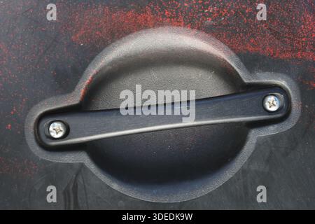 Bouchon rond en plastique noir du réservoir de carburant avec poignée et vis argentée sur fond de texture rouge sale montrant grunge et vue rapprochée de style industriel Banque D'Images