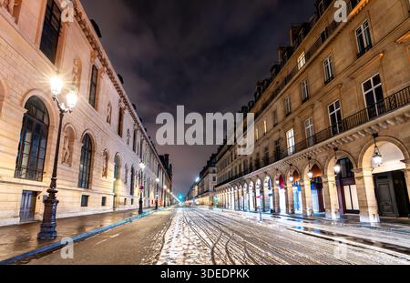Rue de Rivoli se trouve à Paris, France. La scène nocturne hivernale présente de la neige sur la route entre le musée du Louvre et les arcades historiques Banque D'Images