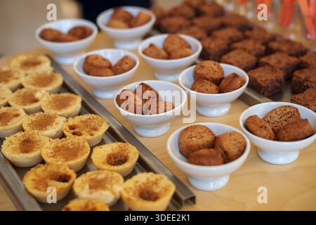 Assortiment de mini tartes et de petites friandises cuites présentées dans des bols et des plateaux sur une table en bois lors d'un buffet ou d'un événement Banque D'Images