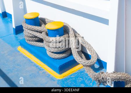 Une vue détaillée d'une corde épaisse attachée autour d'une borne bleue, située sur un bateau près d'un plan d'eau calme. Représente les activités maritimes, la navigation de plaisance et Banque D'Images
