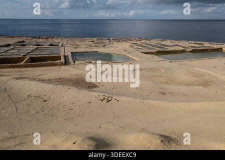 Large vue côtière montrant les marais salants traditionnels surplombant la mer Méditerranée, où les bassins peu profonds, les textures de pierre et l'eau libre créent une balance Banque D'Images