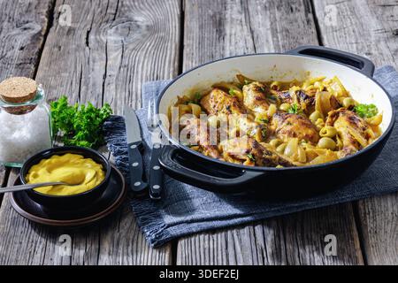 Poulet sénégalais traditionnel Yassa avec pilons braisés, oignons caramélisés et olives vertes dans une poêle sur une table en bois. Authentique Afrique de l'Ouest Banque D'Images