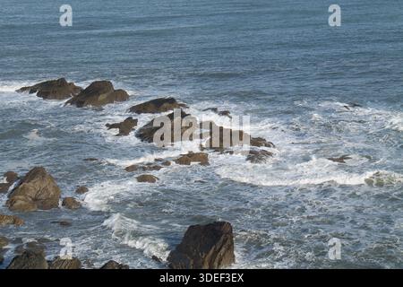 Les vagues se brisent au-dessus des rochers marins côtiers de l'océan. Banque D'Images