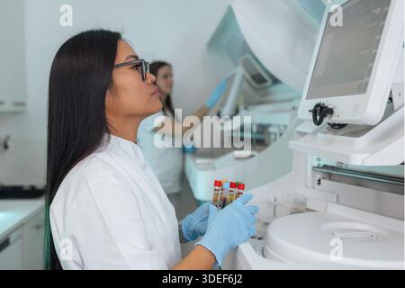 Une femme scientifique mène des travaux de laboratoire pharmaceutique, examinant des tubes à essai tandis qu'une autre scientifique travaille en arrière-plan pendant la recherche. Banque D'Images