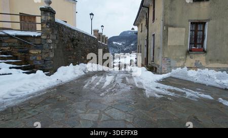Une rue escarpée pavée dans le village italien de Vezzolacca est couverte de neige et de glace, avec des maisons traditionnelles bordant les flancs et les montagnes Banque D'Images
