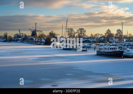 Paysage hivernal de Weesp, port de plaisance, rivière Vecht et moulins à vent traditionnels couverts de neige au coucher du soleil Banque D'Images