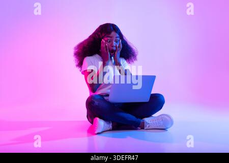 La femme choquée réagit dans la surprise tout en travaillant sur l'ordinateur portable dans le réglage néon lumière Banque D'Images