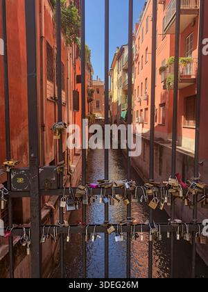 Canal urbain vu à travers une clôture métallique couverte de serrures d'amour, symbolisant la romance, les souvenirs de voyage et la vie urbaine. Bologne, Italie Banque D'Images