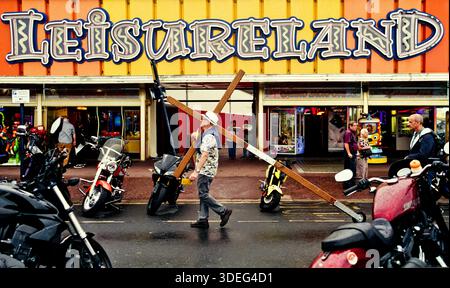 Un homme transporte un crucifix devant la salle de jeux Leiesureland à Great Yarmouth, Norfolk, Royaume-Uni Banque D'Images