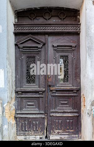Vieille porte double en bois ornée dans un état de délabrement, avec de la peinture écaillée et du bois altéré, des sculptures et des grilles décoratives en fer forgé. Banque D'Images