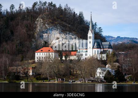 Reflets de Bled – Une vue sereine au bord du lac de l’église emblématique de Bled et de la toile de fond alpine, capturée dans une lumière hivernale éclatante Banque D'Images