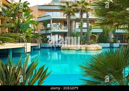 Julian's, Malte - 6 janvier 2026 : piscine turquoise de luxe avec palmiers et plantes tropicales, avec des chambres avec balcon et accès à la nage. Banque D'Images
