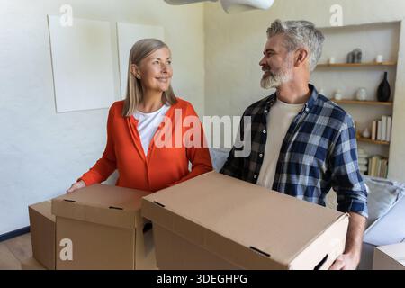 Homme et femme souriant tenant des boîtes dans le salon Banque D'Images