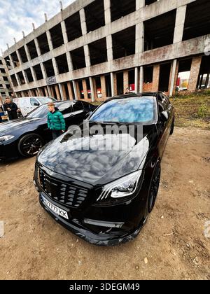 Ternopil, Ukraine - 29 novembre 2025 : Mercedes-Benz classe S Brabus W222 noir élégant sur un terrain de terre à côté d'une structure en béton squelettique avec des spectateurs Banque D'Images