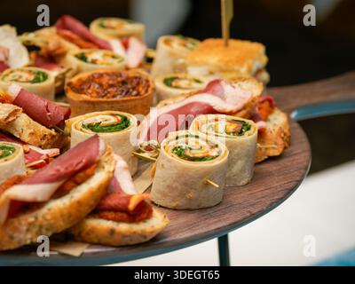Assortiment de grignotines salées comprenant des roulés, des sandwichs et de la charcuterie servis sur une planche de bois lors d'un buffet de restauration. Banque D'Images
