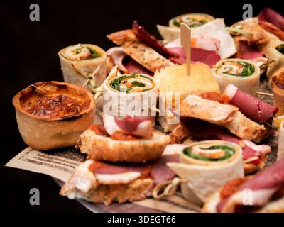 Assortiment de grignotines salées comprenant des roulés, des sandwichs et de la charcuterie servis sur une planche de bois lors d'un buffet de restauration. Banque D'Images