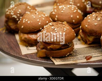 Plateau de mini-cheeseburgers avec petits pains au sésame servis sur une planche de bois lors d'un traiteur intérieur ou d'un buffet. Banque D'Images