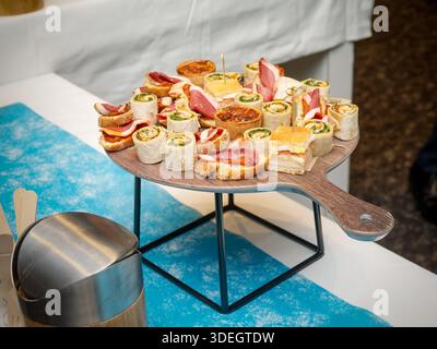 Assortiment de grignotines salées comprenant des roulés, des sandwichs et de la charcuterie servis sur une planche de bois lors d'un buffet de restauration. Banque D'Images