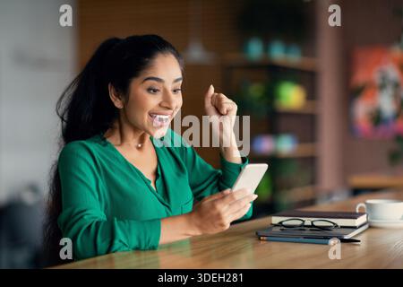 Femme du Moyen-Orient émotive ayant de bonnes nouvelles, en utilisant le téléphone cellulaire Banque D'Images