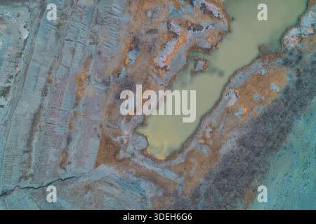 Sombre vue aérienne de dessus d'une piscine d'eau verte sombre dans un site d'excavation industrielle. Le lac pollué entouré d'argile grise érodée et de végétation sèche illustre les dommages environnementaux et la contamination des sols. Copier l'espace. Banque D'Images