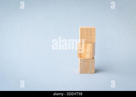 Trois blocs carrés en bois vierges empilés, sur une surface bleu clair. Banque D'Images