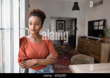 Jeune femme africaine sérieuse et réfléchie debout à la fenêtre Banque D'Images