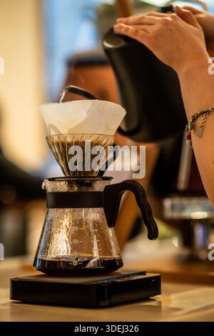 Le barista prépare le café à verser en utilisant une méthode de préparation manuelle avec un équipement spécialisé. De l'eau chaude est versée sur le Marc de café dans un filtre. Banque D'Images