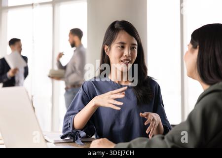Positive jeune femme professionnelle asiatique parlant à une collègue féminine Banque D'Images