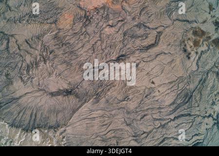 Vue aérienne de haut en bas d'un réseau dense de fissures d'érosion sur un sol argileux gris avec de subtiles traces minérales rougeâtres. Texture de friche industrielle très détaillée ressemblant à des structures organiques microscopiques ou à une dégradation environnementale grave des terres. Banque D'Images