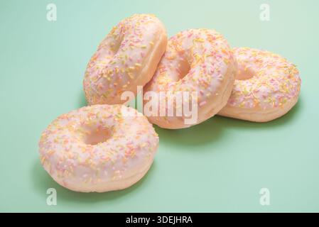 Beignets avec glaçage blanc et miettes de caramel rose sur fond vert Banque D'Images