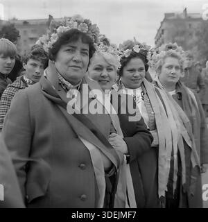 Slaviansk, région de Donetsk, RSS d'Ukraine, Union soviétique, années 1980 Portrait de groupe de quatre femmes adultes, membres d'une chorale folklorique amateur, posant dans une rue de la ville lors d'un défilé de vacances. Ils portent des couronnes florales festives avec de longs rubans fluides sur la tête. Des manteaux chauds d'automne sont portés sur leurs costumes brodés traditionnels, indiquant le temps frais. Les femmes se tiennent bras dans bras, paraissant dignes. En arrière-plan, les spectateurs sont visibles. Cette photo d'archive capture l'esprit authentique de la vie culturelle soviétique dans le Donbass paisible. Banque D'Images