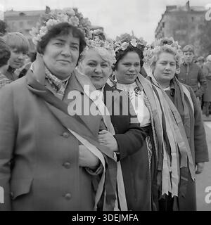 Slaviansk, région de Donetsk, RSS d'Ukraine, Union soviétique, années 1980 Portrait de groupe de quatre femmes adultes, membres d'une chorale folklorique amateur, posant dans une rue de la ville lors d'un défilé de vacances. Ils portent des couronnes florales festives avec de longs rubans fluides sur la tête. Des manteaux chauds d'automne sont portés sur leurs costumes brodés traditionnels, indiquant le temps frais. Les femmes se tiennent bras dans bras, paraissant dignes. En arrière-plan, les spectateurs sont visibles. Cette photo d'archive capture l'esprit authentique de la vie culturelle soviétique dans le Donbass paisible. Banque D'Images