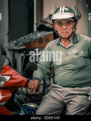 Nha Trang, Vietnam, 27 septembre 2025. Vieux Grab Driver pose sur Red Scooter au Vietnam Banque D'Images