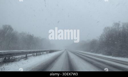 Vue à travers le pare-brise d'une voiture particulière conduisant dans la neige légère sur une autoroute vide, partiellement adaptée, sans circulation avec des voies couvertes Banque D'Images