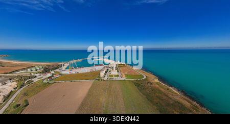 Panorama drone du port de Vasto sur la côte Adriatique avec des cargos, de petits bateaux, des installations portuaires industrielles, des champs ruraux, et la mer Azur sous un Banque D'Images