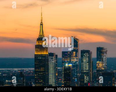 Vue aérienne de l'Empire State Building et des gratte-ciels modernes traversant le ciel crépusculaire, leurs lumières scintillant contre les villes sombres Banque D'Images