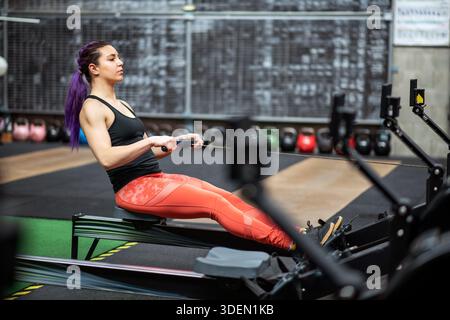 Femme athlétique effectuant un entraînement complet du corps sur une machine à ramer dans une installation de fitness Banque D'Images