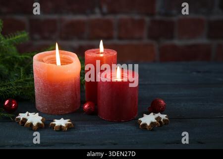 Bougies rouges d'arbre, quelques biscuits, boules et branches de sapin contre un mur de briques foncées, décoration ou carte de voeux pour Noël, l'Avent ou le nouvel an, grand espace de copie, soft focus sélectionné Banque D'Images