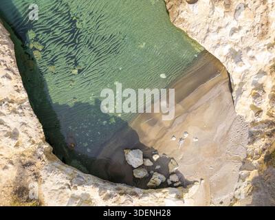 Vue aérienne des grottes de Papafragas, où les eaux turquoises rencontrent les falaises beiges et le rivage sablonneux, créant un contraste saisissant de couleurs et de textes Banque D'Images