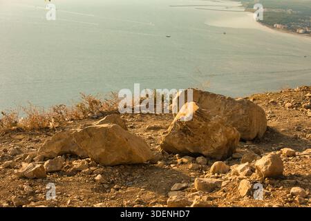 De grands rochers ensoleillés reposent sur une pente de montagne sèche surplombant la côte de Vlora, en Albanie. Photographié le 17 août 2025 Banque D'Images