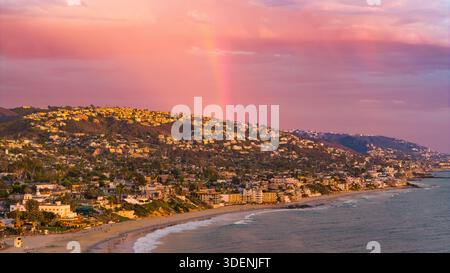 Vue aérienne d'un arc-en-ciel voûtant sur les maisons côtières et la plage de sable, le ciel peint avec des teintes pastel, comme l'océan rencontre le rivage, Laguna Beach, Banque D'Images