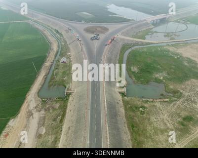 Vue aérienne d'une intersection en y de routes nouvellement construites coupant à travers le paysage, créant un contraste frappant avec la verdure environnante, Mithamain Banque D'Images
