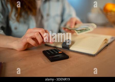 Mains de la personne organisant l'argent, en utilisant une calculatrice, et examinant un cahier pour la budgétisation et le paiement des factures de services publics, mettant l'accent sur la planification financière et la gestion de l'argent Banque D'Images