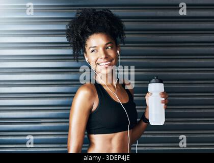 Pensée, bouteille d'eau et femme au gymnase avec de la musique pour l'entraînement, l'entraînement et l'exercice. Sports, écouteurs et personne heureuse pour l'hydratation, la soif et Banque D'Images