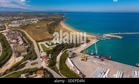 Tir par drone à grand angle capturant l'infrastructure portuaire de Vasto, les navires amarrés, les fourgonnettes et les pales d'éoliennes le long des eaux bleues calmes de l'Adriatique coa Banque D'Images