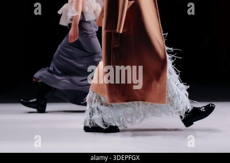 Manteau brun satiné chic et bottes noires, tenues de luxe de femme de mode, deux modèles de mode marchant le défilé de mode Runway Banque D'Images