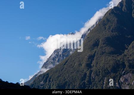 Un sommet majestueux de montagne partiellement couvert de nuages sous un ciel bleu clair. Les pentes verdoyantes contrastent avec les falaises rocheuses, créant un magnifique Banque D'Images