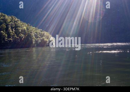 Un paysage serein avec un plan d'eau calme entouré de collines verdoyantes. Les rayons du soleil rayonnent à travers la scène, créant une atmosphère tranquille Banque D'Images